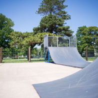 A bright skate park with ramps, surrounded by trees and a blue sky, evokes excitement and a sense of adventure.