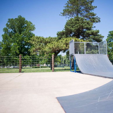 A bright skate park with ramps, surrounded by trees and a blue sky, evokes excitement and a sense of adventure.