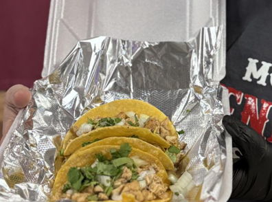 Three tacos in a takeout container, filled with chicken, cilantro, and onions in yellow corn tortillas, evoke comfort and craving.