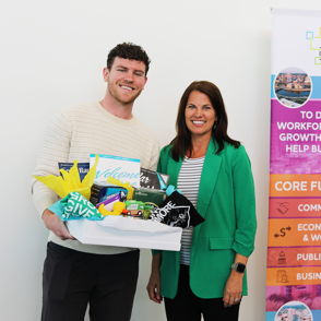 Two smiling individuals hold a large box of items, celebrating economic growth and community development together.