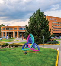 Well-kept outdoor area with a colorful sculpture, green grass, and landscaped flowerbeds, evoking tranquility and community.