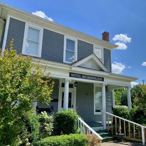 A charming gray house with white trim and a front porch, surrounded by greenery, under a sunny blue sky. Inviting and nostalgic.