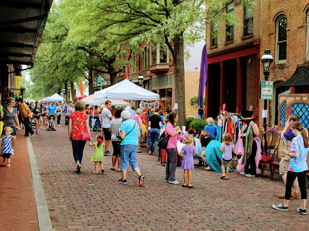 A vibrant street fest with families enjoying stalls, games, and greenery, evoking joy, community, and celebration.