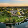 Aerial view of a serene house on a lush island, featuring a pool, surrounded by greenery and reflecting a warm sunset.