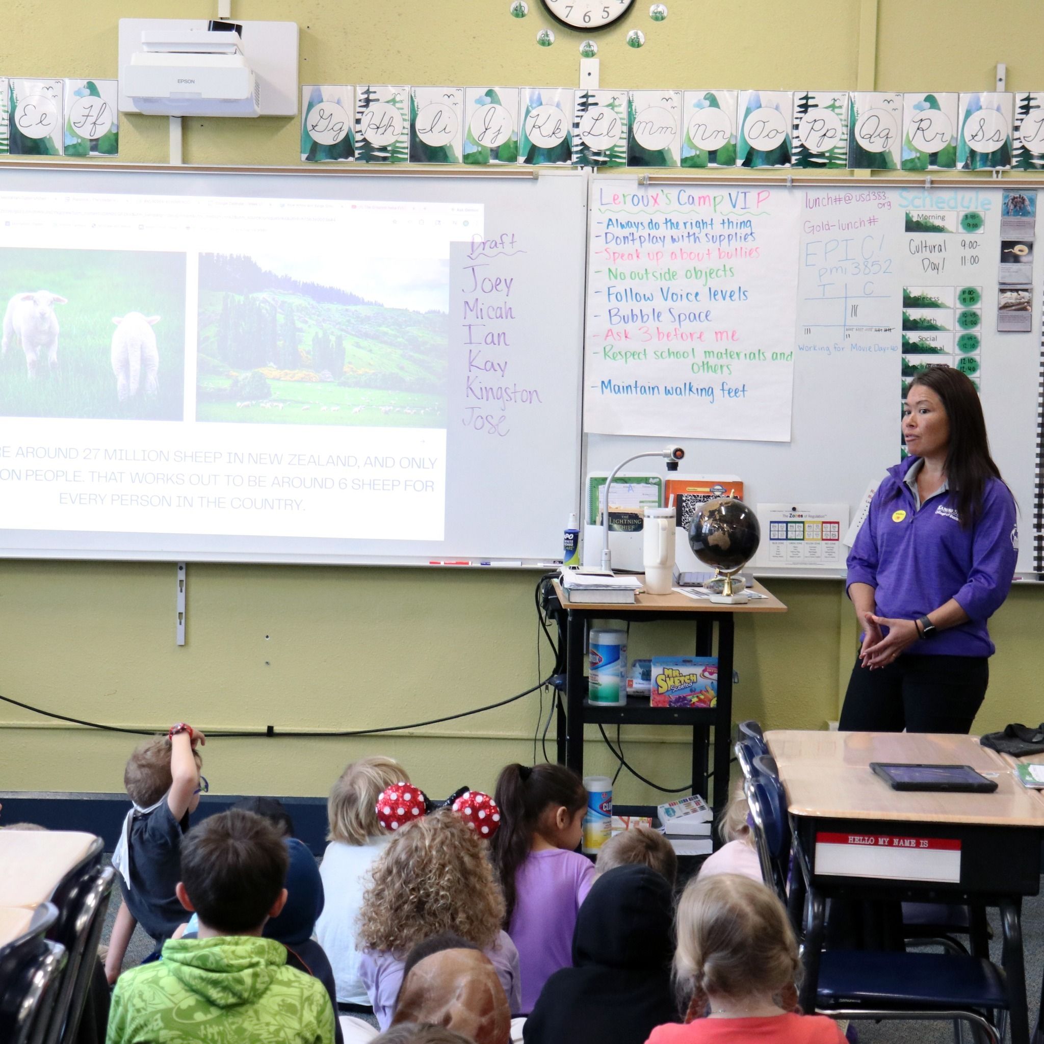 A teacher engages attentive young students in a bright classroom, presenting nature-related images on a projector screen.