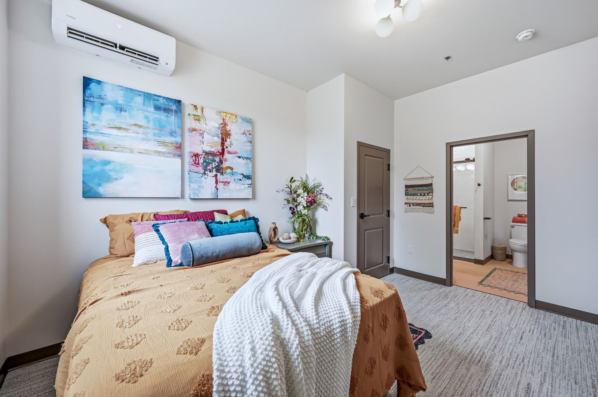 Cozy bedroom with a mustard duvet, colorful pillows, vibrant abstract art, and warm lighting, evoking comfort and tranquility.