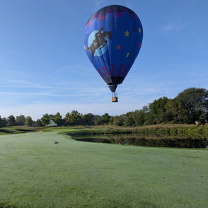 Colorful hot air balloon over lush landscape and water; clear sky evokes joy, adventure, and tranquility.