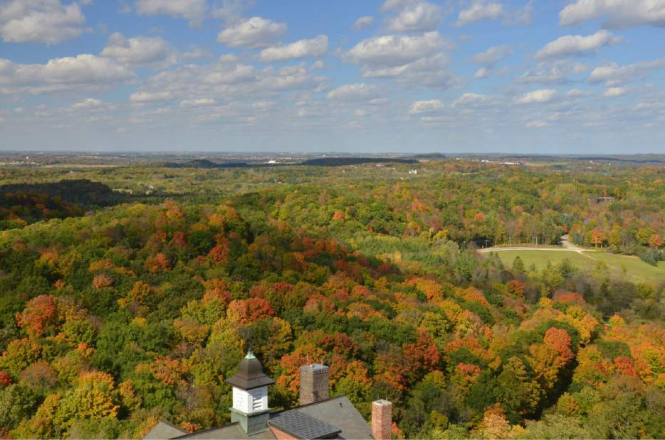 Vibrant fall landscape with colorful trees and clouds, highlighting a building, evoking tranquility and appreciation for nature.