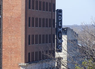 An urban scene features the historic "THE DEMING" building amidst clear skies and bare branches, evoking nostalgia and serenity.