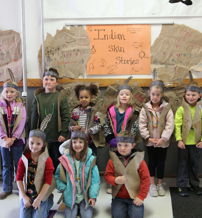 Children in costumes pose in a cheerful classroom, celebrating Indigenous culture with a "Indian Star Stories" banner and crafts.