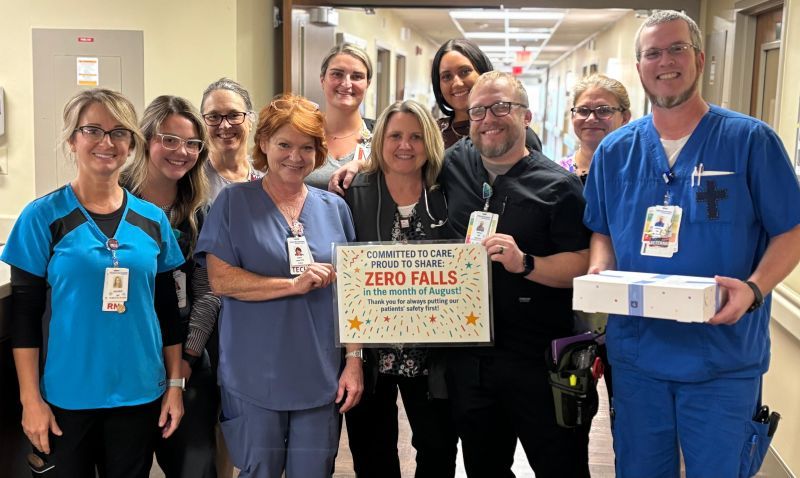 Healthcare professionals celebrate achieving "ZERO FALLS!" in a hospital corridor, posing with smiles and a treat box.