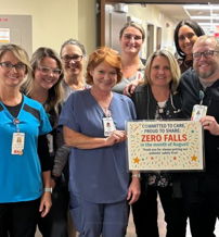 Healthcare professionals celebrate achieving "ZERO FALLS!" in a hospital corridor, posing with smiles and a treat box.