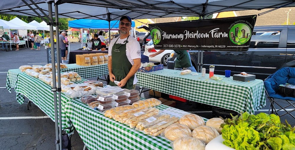 A friendly vendor showcases baked goods at a vibrant farmers' market, surrounded by colorful stalls and a lively atmosphere.