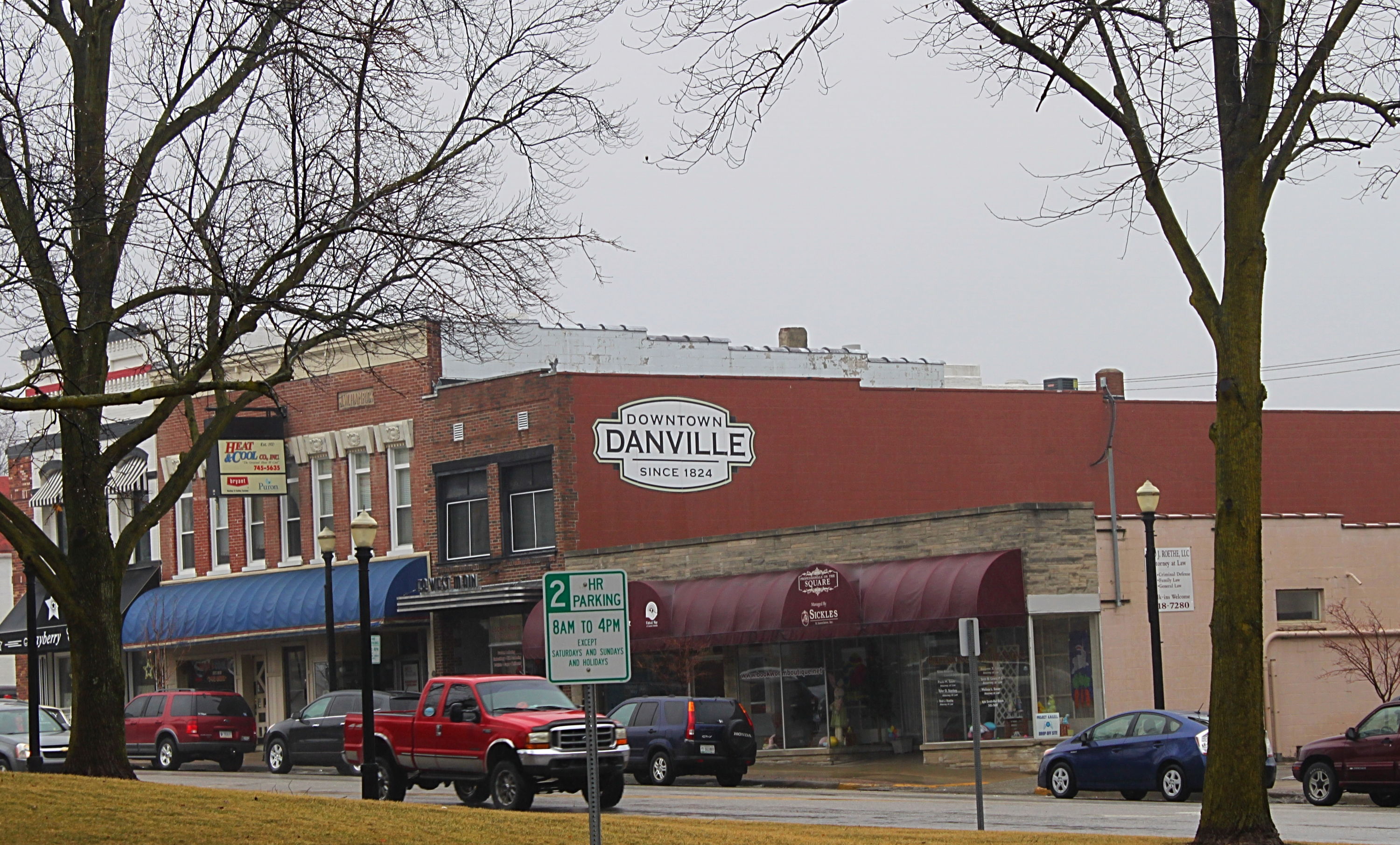 A quaint small town street scene features vintage storefronts, parked cars, and a calm, nostalgic atmosphere under gray skies.