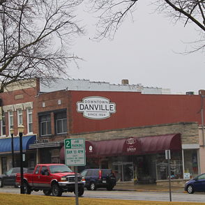 A quaint small town street scene features vintage storefronts, parked cars, and a calm, nostalgic atmosphere under gray skies.