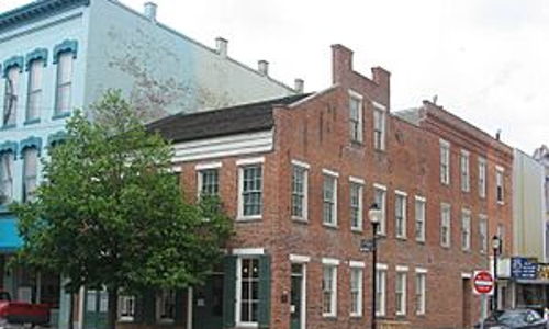 A charming brick building at a street corner, surrounded by varied architecture and a small tree, evokes warmth and nostalgia.