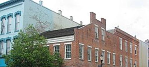 A charming brick building at a street corner, surrounded by varied architecture and a small tree, evokes warmth and nostalgia.