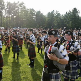Outdoor gathering of people in kilts playing bagpipes, celebrating tradition and community amidst vibrant greenery.