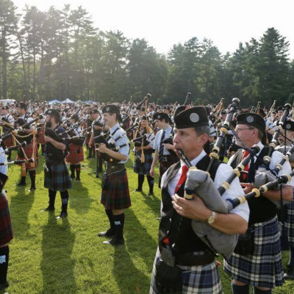 Outdoor gathering of people in kilts playing bagpipes, celebrating tradition and community amidst vibrant greenery.