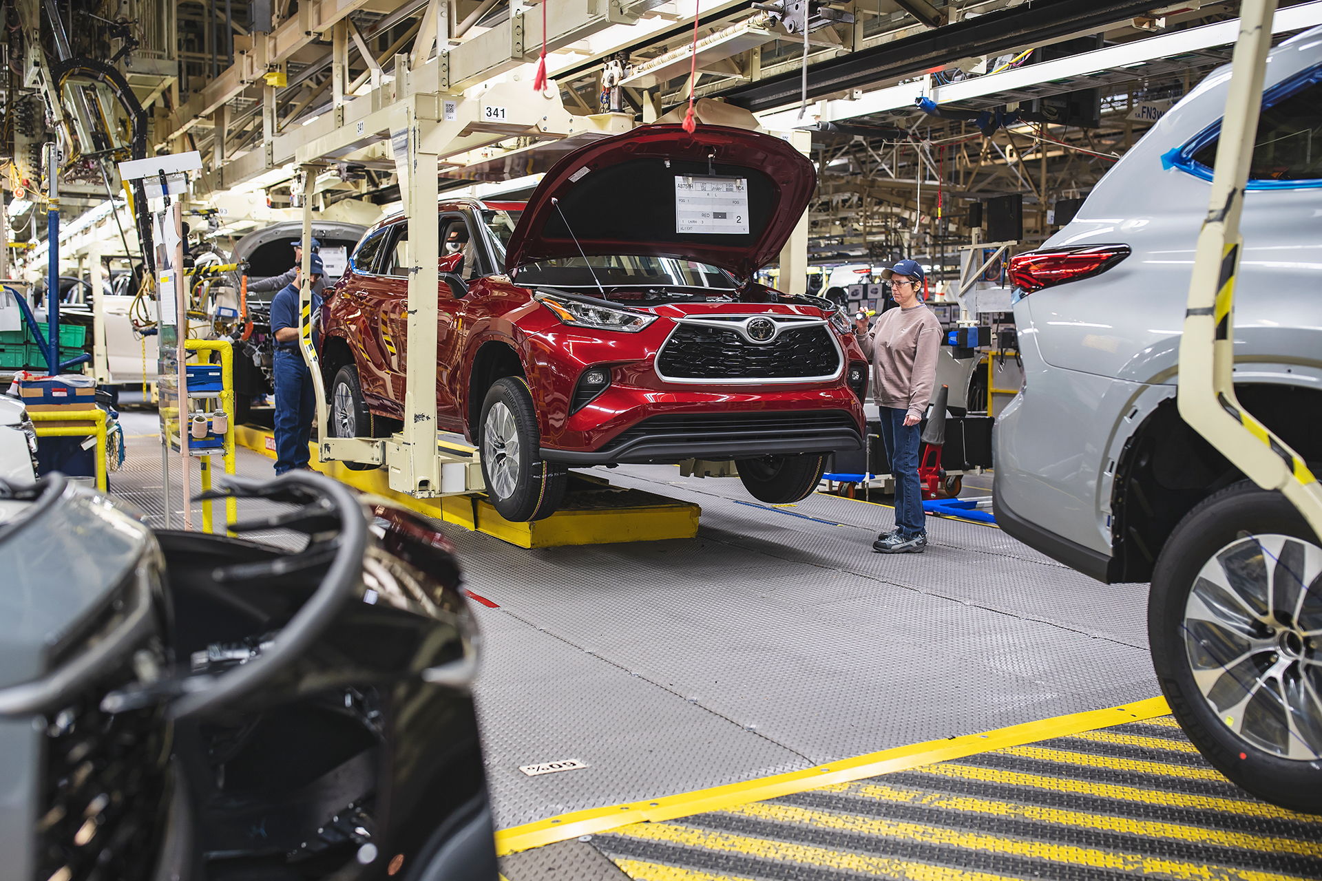 A busy car assembly line with a red car elevated for inspection, showcasing teamwork and modern manufacturing efficiency.