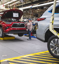 A busy car assembly line with a red car elevated for inspection, showcasing teamwork and modern manufacturing efficiency.