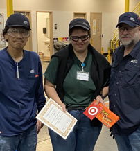 Three individuals in work attire celebrate an achievement, holding a certificate and a logo bag, showcasing teamwork and pride.