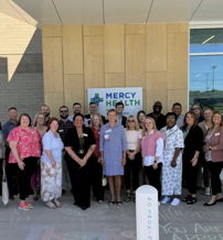 Group of smiling people in professional attire outside "Mercy Health," conveying positivity, unity, and a sense of community.