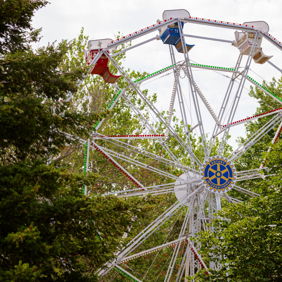 Colorful Ferris wheel with red, green, and blue seats peeks through trees, evoking nostalgia and joy from fairgrounds.