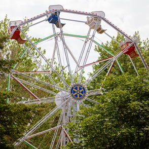 Colorful Ferris wheel with red, green, and blue seats peeks through trees, evoking nostalgia and joy from fairgrounds.