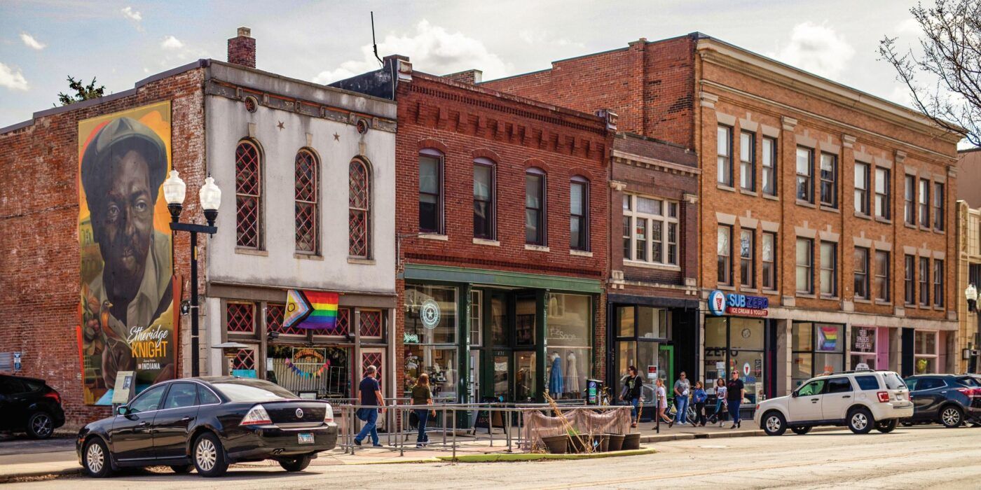 Vibrant street scene with charming brick buildings, a mural, rainbow flag, and lively community atmosphere.