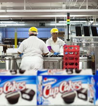 Workers in a food production facility assemble cupcakes in a clean, organized space, highlighting teamwork and productivity.