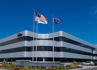 Modern office building with glass exterior, flags, clear sky; evokes professionalism, optimism, and a positive work environment.