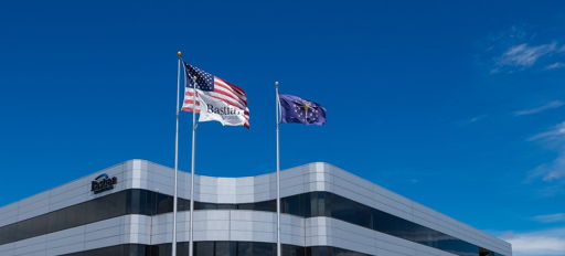 Modern office building with glass exterior, flags, clear sky; evokes professionalism, optimism, and a positive work environment.
