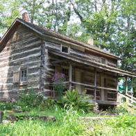 A rustic log cabin in a lush green landscape, surrounded by vibrant vegetation, evokes nostalgia and tranquility.