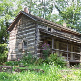 A rustic log cabin in a lush green landscape, surrounded by vibrant vegetation, evokes nostalgia and tranquility.