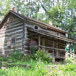 A rustic log cabin in a lush green landscape, surrounded by vibrant vegetation, evokes nostalgia and tranquility.