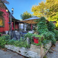 Charming outdoor dining area at a vibrant red café, surrounded by green plants, bright skies, and a cozy ambiance.