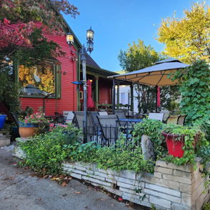 Charming outdoor dining area at a vibrant red café, surrounded by green plants, bright skies, and a cozy ambiance.