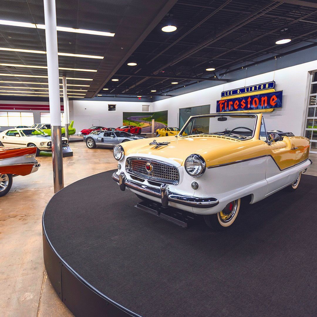 A vintage yellow and white convertible shines in a classic car showroom filled with polished vehicles, evoking nostalgia.