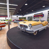 A vintage yellow and white convertible shines in a classic car showroom filled with polished vehicles, evoking nostalgia.