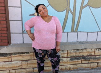 A woman in a pink sweater stands confidently by a colorful leaf mural, exuding happiness and a cheerful atmosphere.