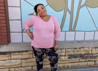 A woman in a pink sweater stands confidently by a colorful leaf mural, exuding happiness and a cheerful atmosphere.