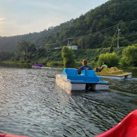A serene sunset scene with people on paddle boats in calm waters, surrounded by lush hills, evoking tranquility and joy.