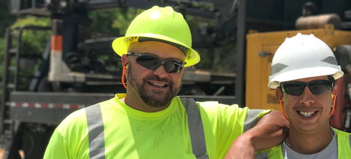 Two smiling workers in safety gear at a construction site, highlighting teamwork, positivity, and fulfillment in their work.