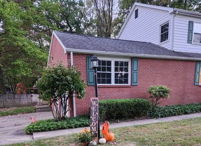 Cozy brick house with green shutters, pumpkins, and seasonal decor, evoking warmth and nostalgia for fall.