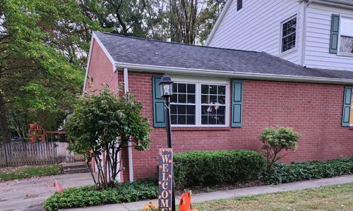Cozy brick house with green shutters, pumpkins, and seasonal decor, evoking warmth and nostalgia for fall.
