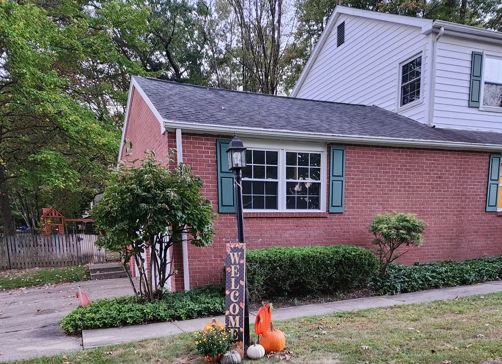 Cozy brick house with green shutters, pumpkins, and seasonal decor, evoking warmth and nostalgia for fall.