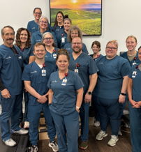 A group of friendly healthcare professionals in teal scrubs, showcasing teamwork and positivity in a rehab clinic.
