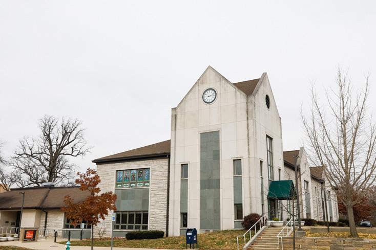 Modern building with a pointed roof, clock, and neutral tones, surrounded by bare trees under an overcast sky, evoking calmness.