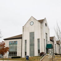 Modern building with a pointed roof, clock, and neutral tones, surrounded by bare trees under an overcast sky, evoking calmness.